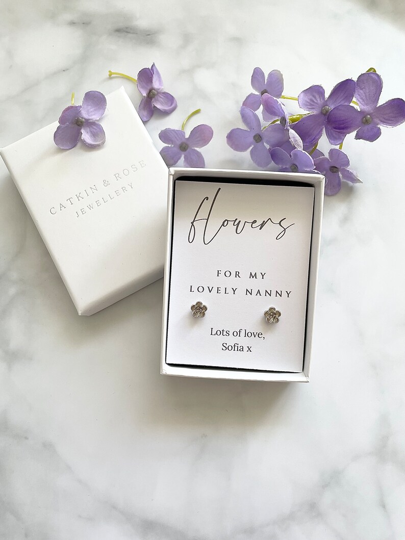 May include: A white gift box with a silver flower earring set inside. The box has a white label with the text "Flowers for my lovely nanny" and "Lots of love, Sofia x".