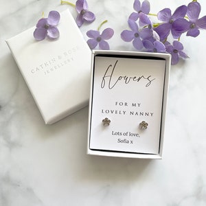 May include: A white gift box with a silver flower earring set inside. The box has a white card with the text "Flowers for my lovely nanny. Lots of love, Sofia x".