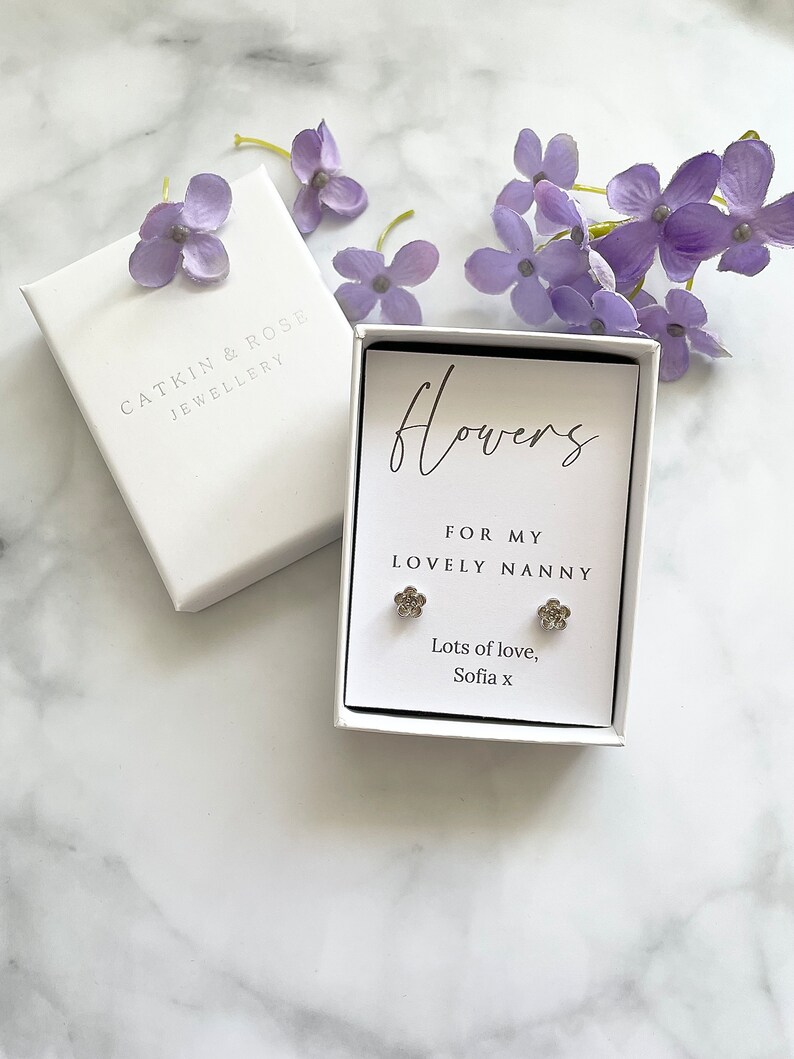 May include: A white gift box with a silver flower earring set inside. The box has a white card with the text "Flowers for my lovely nanny. Lots of love, Sofia x".