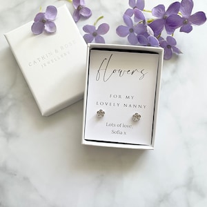 May include: A white gift box with a silver flower earring set inside. The box has a white card with the text "Flowers for my lovely nanny. Lots of love, Sofia x".