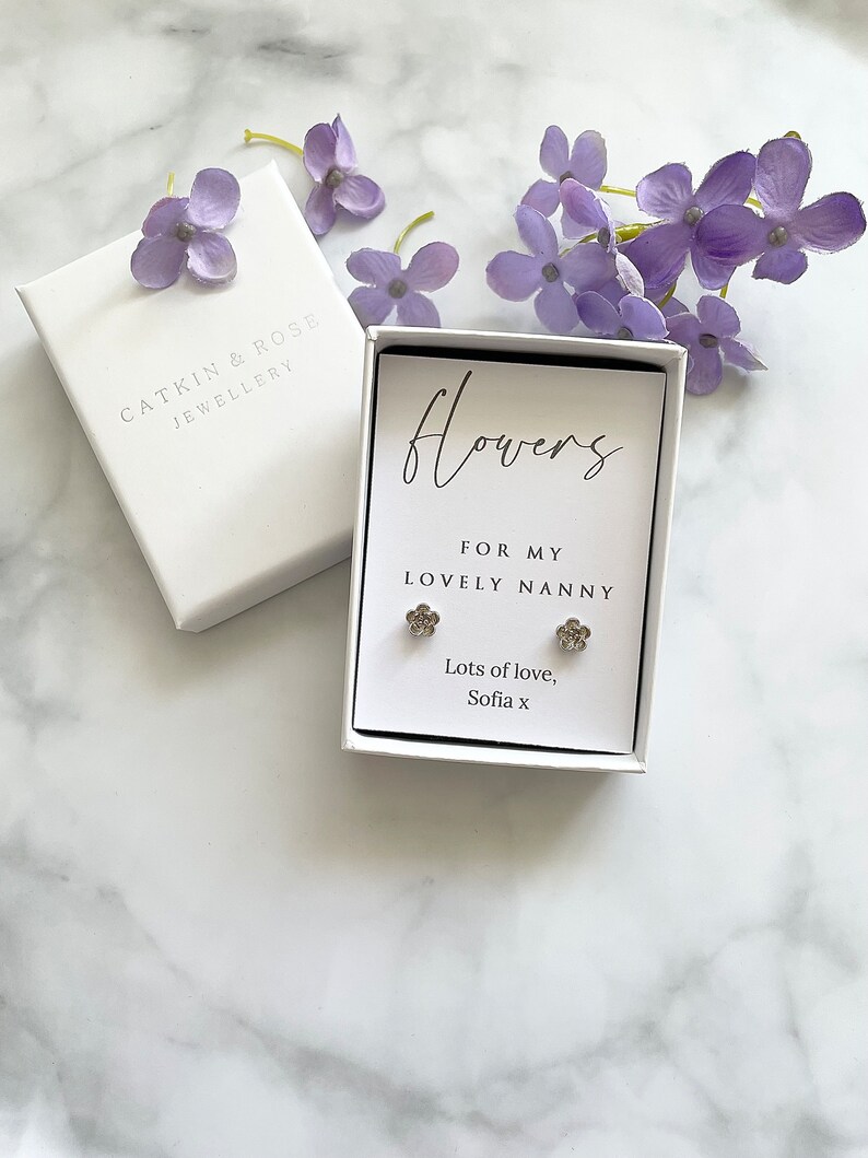 May include: A white gift box with a silver flower earring set inside. The box has a white card with the text "Flowers for my lovely nanny. Lots of love, Sofia x".