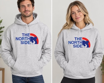 May include: A light grey hooded sweatshirt featuring a graphic on the chest with the text THE NORTH SIDE in blue, accompanied by a blue bear silhouette partially enclosed within a red and blue semi-circular arch design on the right side.