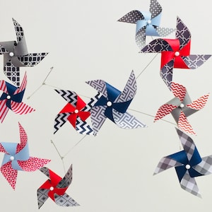 May include: A mobile with nine pinwheels in various patterns. The pinwheels are red, blue, gray, and white. The pinwheels are suspended from a metal frame.