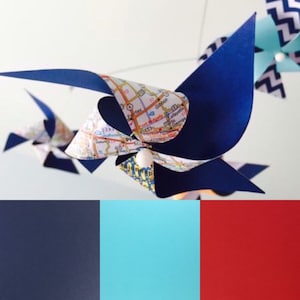 Peut inclure: Une palette de couleurs bleu, rouge et turquoise avec un mobile en forme de moulin à vent à thème de carte. Le moulin à vent est fait de papier et a une carte d'une ville imprimée dessus. Le moulin à vent est suspendu à une ficelle et pend au plafond.