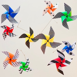 May include: A mobile with 10 colorful pinwheels, each with a different geometric pattern. The pinwheels are made of paper and have black and white accents. The mobile is suspended from the ceiling.