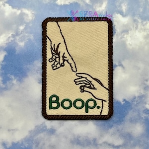 May include: A brown and white embroidered patch with a green 'Boop' text and a depiction of two hands reaching towards each other, similar to the famous 'Creation of Adam' painting.