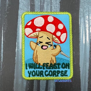 May include: A green and blue embroidered patch with a cartoon mushroom holding a knife. The mushroom has a red and white cap and is crying. The text on the patch reads "I will feast on your corpse".