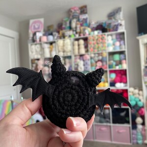 May include: A black crocheted bat with fabric wings. The bat is a small, handmade toy.