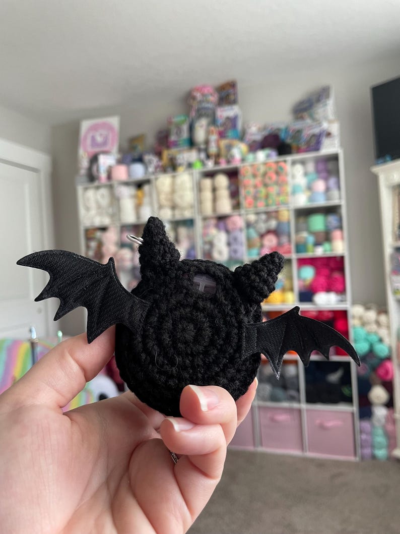May include: A black crocheted bat with fabric wings. The bat is a small, handmade toy.
