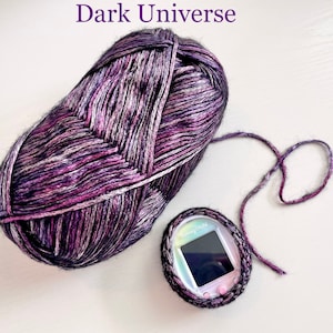 Pode incluir: Uma bola de fio roxo e preto com um brilho prateado, etiquetada como "Dark Universe". Uma pequena bolsa cinza de croch&ecirc; com um brinquedo digital para animais de estima&ccedil;&atilde;o dentro.