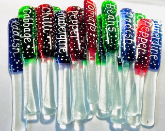 May include: A set of 14 glass plant markers with white polka dots and white lettering. The markers are in three colors: red, green, and blue. The lettering on the markers includes the names of vegetables: radish, cabbage, chili, aubergine, pepper, tomato, beans, radish, pepper, and cucumber.