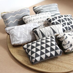 May include: A collection of eight small zippered pouches with various geometric patterns in black and white on a light gray background. The pouches are arranged in a circle on a wooden surface.