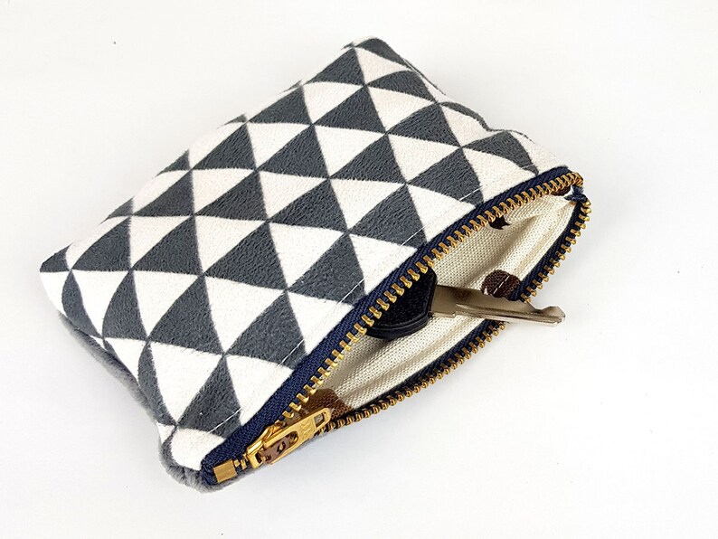 May include: A small zippered pouch with a white and gray geometric pattern. The pouch is open and a key is inside.