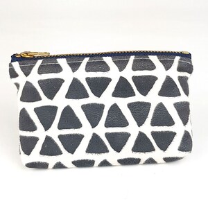 May include: A small, white zippered pouch with a geometric pattern of gray triangles. The pouch is made of a soft, textured fabric.