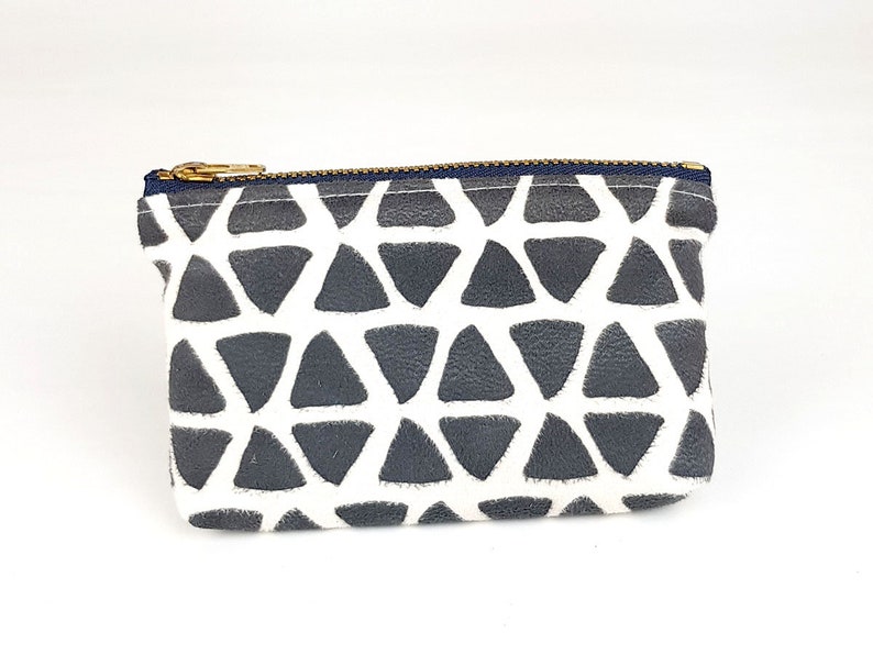 May include: A small, white zippered pouch with a geometric pattern of gray triangles. The pouch is made of a soft, textured fabric.