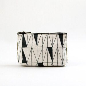 May include: A small white zippered pouch with a black and white geometric pattern. The pattern features a series of triangles and lines.