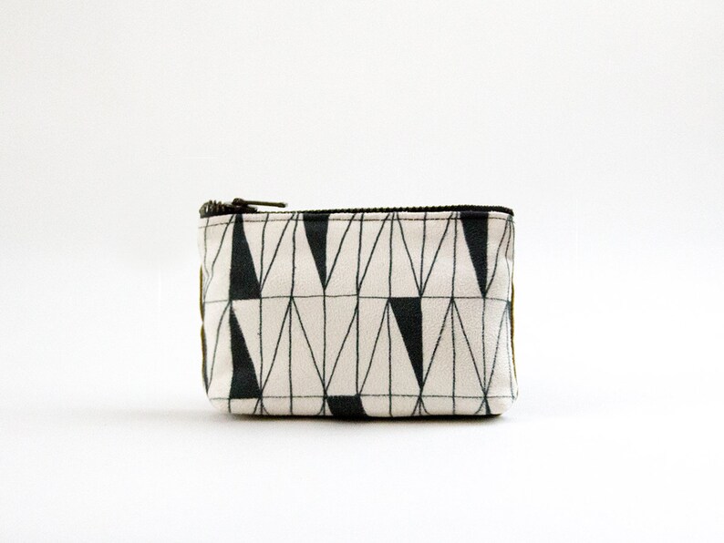 May include: A small white zippered pouch with a black and white geometric pattern. The pattern features a series of triangles and lines.