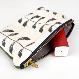 May include: A small zippered pouch with a white background and a black leaf pattern. The pouch is open and a red and white tube is inside.