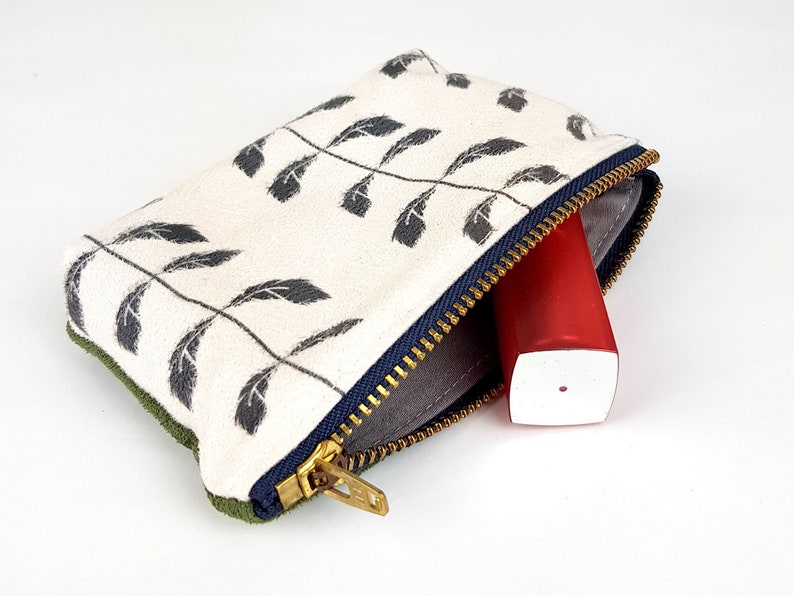 May include: A small zippered pouch with a white background and a black leaf pattern. The pouch is open and a red and white tube is inside.