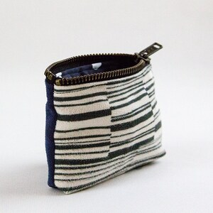 May include: A small zippered pouch with a white and black striped fabric exterior and a navy blue fabric lining. The zipper is metal and has a silver finish.