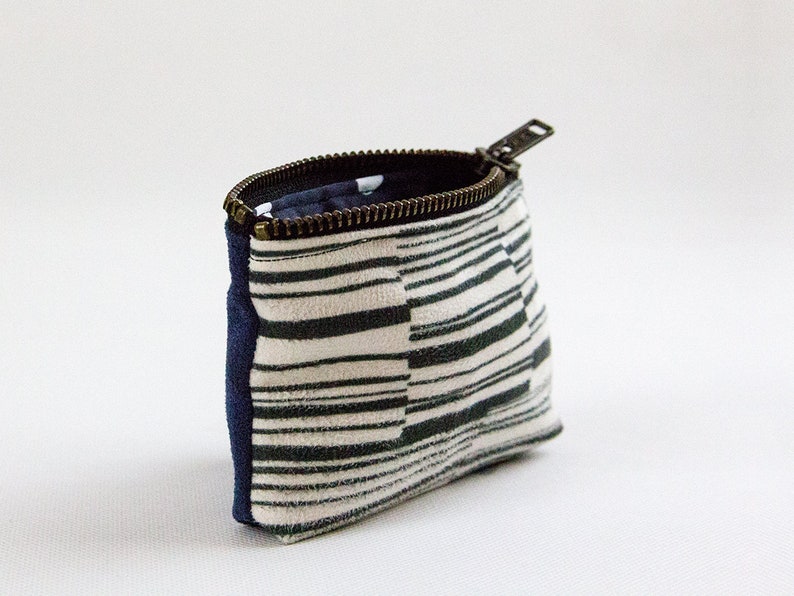 May include: A small zippered pouch with a white and black striped fabric exterior and a navy blue fabric lining. The zipper is metal and has a silver finish.