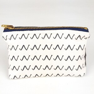 May include: A white canvas zippered pouch with a black and white zig-zag pattern.
