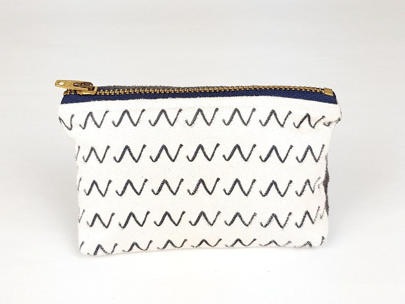 May include: A white canvas zippered pouch with a black and white zig-zag pattern.