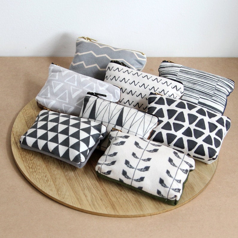 May include: A set of eight small zippered pouches with various geometric patterns in black and white on a light gray background. The pouches are arranged on a wooden surface.