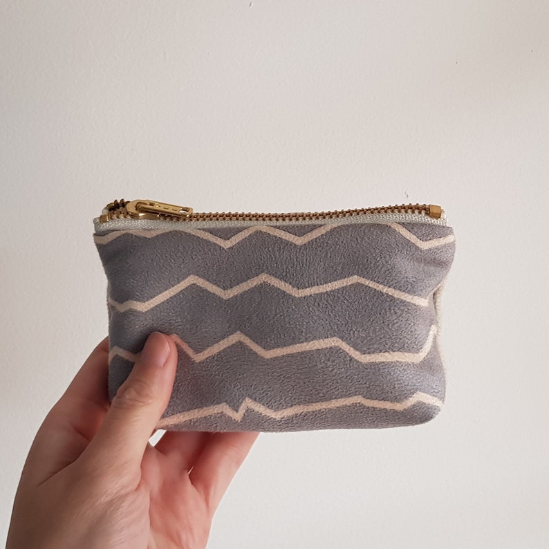 May include: A small gray zippered pouch with a white zig-zag pattern. The pouch is made of a soft, textured fabric.