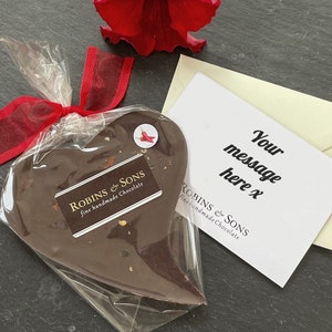 May include: A heart-shaped chocolate treat wrapped in clear cellophane and tied with a red ribbon. The chocolate has a label that reads "ROBINS & SONS fine handmade Chocolate". A card with the text "Your message here x" is included.