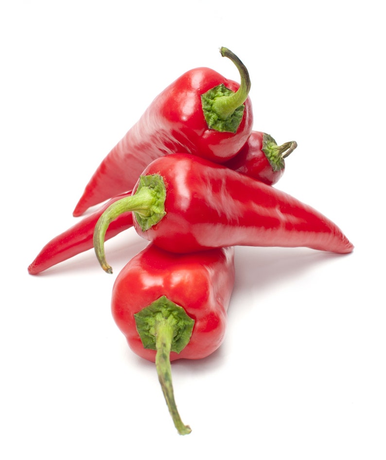May include: A close-up shot of several vibrant red chili peppers, each with a green stem. The peppers are stacked on top of each other against a clean white background. The peppers have a smooth, glossy texture.