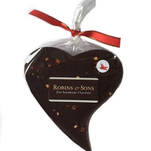 May include: A heart-shaped dark chocolate treat, sprinkled with visible flakes, is wrapped in clear cellophane and tied with a red ribbon. The chocolate has a sticker with a chili pepper image and a label that reads "Robins & Sons fine handmade chocolate."