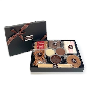 May include: A black gift box tied with a brown ribbon, filled with sweet treats. It includes biscuits, pretzels, marshmallows, chocolate dips, and wooden skewers. The box is labelled "Bonbons & Scones".
