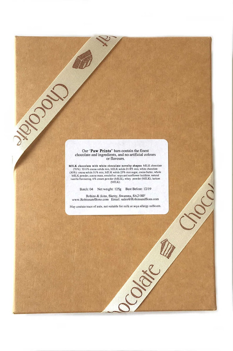 May include: A brown cardboard box tied with a cream ribbon printed with the word "Chocolate". The box contains a label with text about the ingredients of the "Paw Prints" chocolate bars. The ribbon has a small cake graphic.
