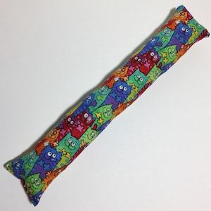 May include: A long, colorful cat-themed toy for cats. The toy is made of fabric and is filled with catnip. The fabric is covered in a pattern of colorful cats.