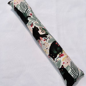 May include: A long, cylindrical catnip toy with a white background and a black cat pattern. The catnip toy is filled with catnip and is designed to be a fun and engaging toy for cats.