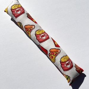 May include: A white fabric hot dog and pizza themed catnip toy. The toy is shaped like a long, thin pillow with a red and white pattern of hot dogs, french fries, and pizza slices. The words "HOT" are printed on the red containers of french fries.