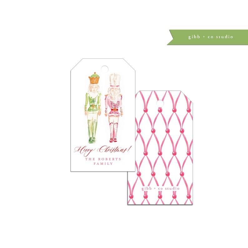 May include: A white gift tag with a watercolor illustration of a nutcracker couple. The tag has the text "Happy Christmas!" and "The Roberts Family" printed on it. The back of the tag has a pink and white ribbon pattern.