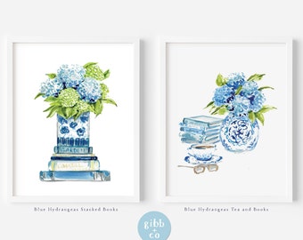 May include: Two watercolor illustrations of blue hydrangeas in blue and white vases. The first image shows a vase on top of a stack of books with the words "GARDEN" and "COASTAL" visible. The second image shows a vase with a stack of books, a teacup, and glasses.