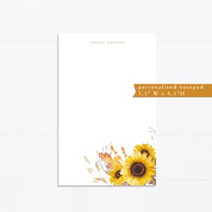 May include: Personalized notepad with the name "EMERY GARNER" printed at the top. The notepad features a watercolor illustration of sunflowers and dried grasses in shades of yellow, brown, and white. The notepad measures 5.5 inches wide by 8.5 inches high.