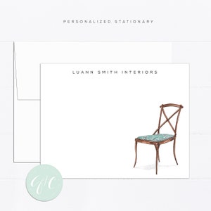 May include: A white card with the text "LUANN SMITH INTERIORS" printed in black. A watercolor illustration of a brown wooden chair with a teal patterned cushion is in the bottom right corner of the card.