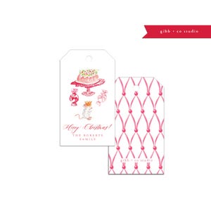 May include: Pink and white Christmas gift tag with a watercolor illustration of a mouse wearing a crown, a cake, and candy. The text "Happy Christmas! The Roberts Family" is printed on the tag.