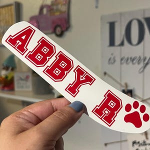 May include: White vinyl sticker with the name "Abby R" in red block letters with a red paw print.