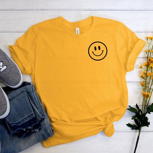 May include: A yellow t-shirt with a black smiley face graphic on the left chest.