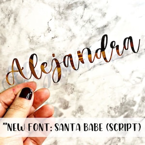 May include: Gold vinyl sticker with the name "Alejandra" written in a cursive font called "Santa Babe (Script)".