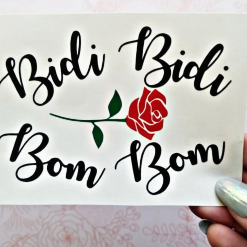 May include: A white background with black cursive text that reads "Bidi Bom" on the left and "Bidi Bom" on the right. A red rose with a green stem and leaves is centered between the text.