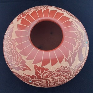 May include: A terracotta-colored, round ceramic vase with a wide opening. The exterior features a carved floral design with a lighter, natural clay color. The vase has a diameter of approximately 10 inches.