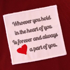 May include: A white square patch with grey embroidered text and a red heart. The text reads: "Whoever you hold in the heart of you is forever and always a part of you."