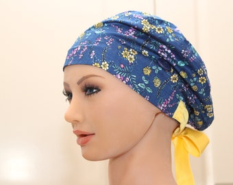 May include: A blue floral print surgical cap with a yellow tie. The cap has a button on the side.