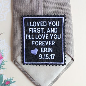 May include: A black and white embroidered patch with the text "I loved you first, and I'll love you forever Erin 9.15.17" in white thread. A small purple heart is above the name.